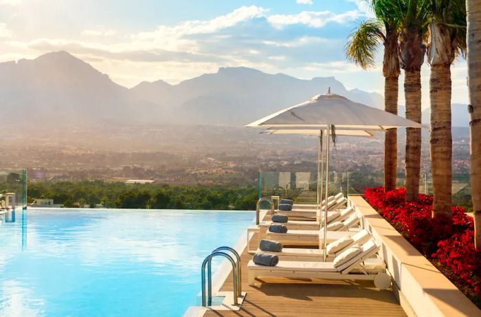 Infinity pool with empty white lounge chairs overlooking distant mountains at Sha Wellness Clinic