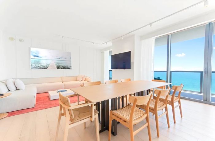 The suite's living area at W South Beach boasts hardwood floors, a spacious white couch, a vibrant pink carpet, and a large light wood dining table.