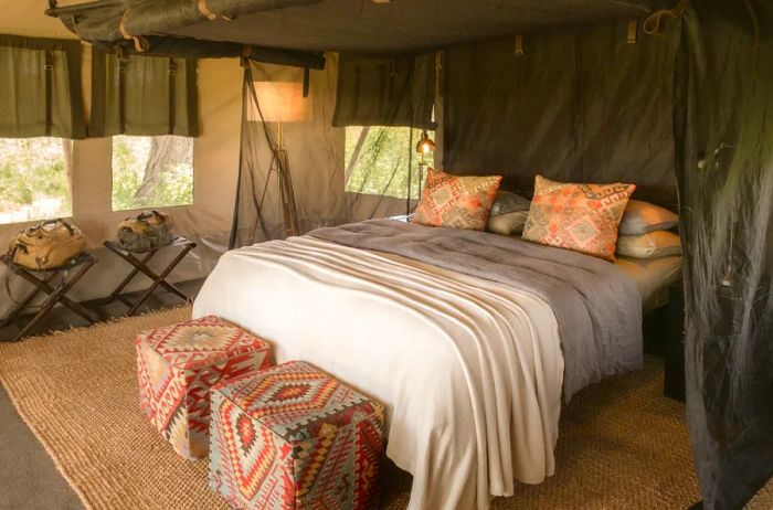 A guest room at Nyasi Tented Camp, featuring canvas walls and windows, adorned with vibrant, patterned pillows and decor.