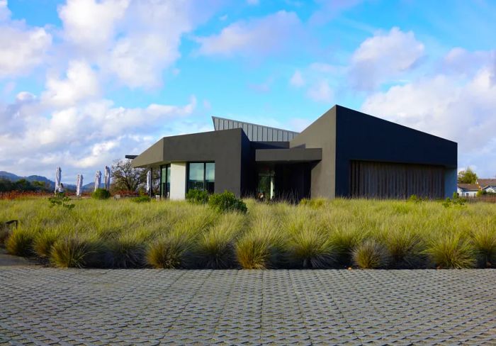 A modern gray exterior of Aperture Winery, framed by tall grass.