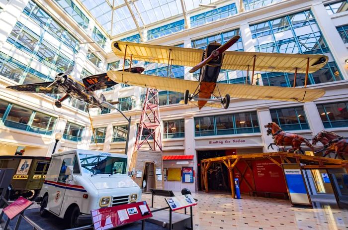 The atrium of the Smithsonian's National Postal Museum, showcasing replicas of a plane, mail truck, and horse-drawn carriage.