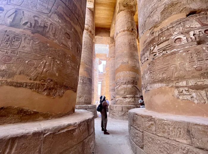 The author stands in awe beneath towering pillars adorned with hieroglyphics in the Karnak temple complex.