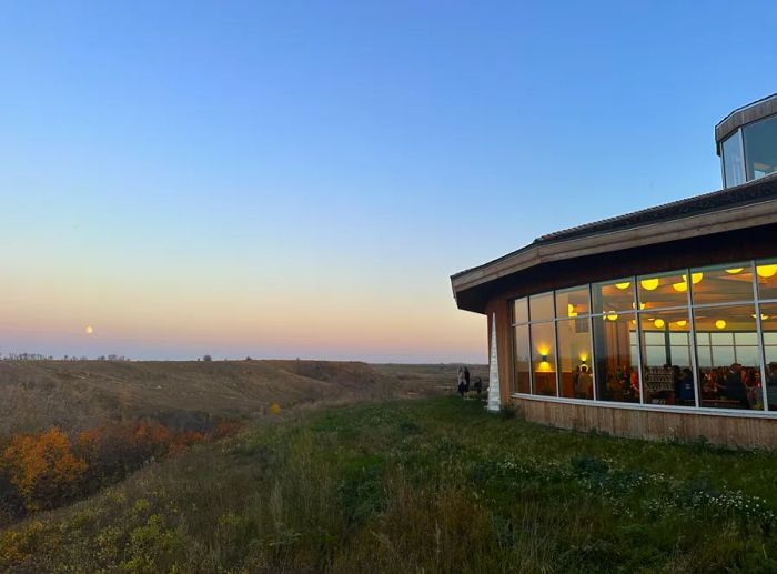 A rounded structure with glass facades overlooking a field and a gently sloping cliff.