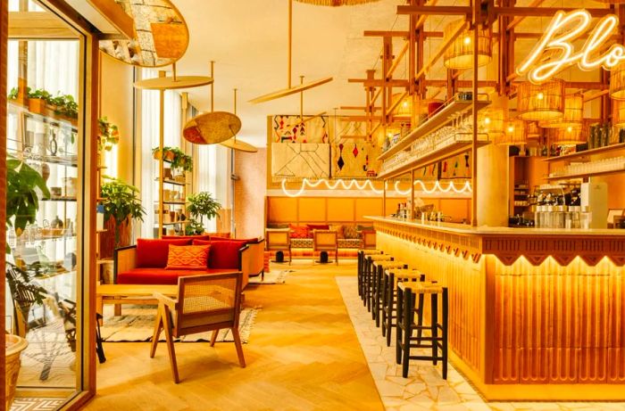 The lobby bar of the Bloom House Hotel & Spa, featuring hardwood floors, rattan-backed chairs, and elegant basket chandeliers.