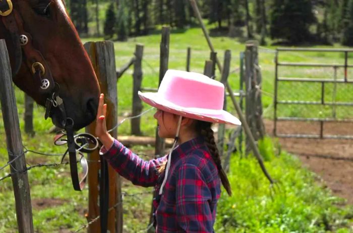 A young girl in a pink cowboy hat gently pets a horse's nose.