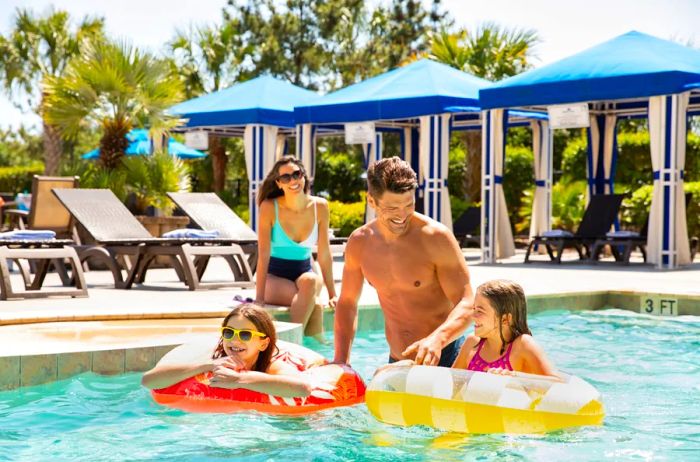 A family enjoying time at a pool, with children floating in inner tubes at North Beach Resort Villas in Myrtle Beach, South Carolina.