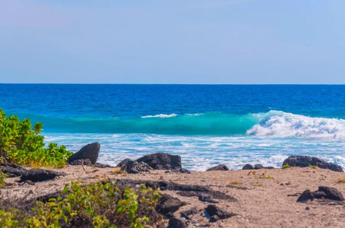 Waves crashing against a sandy shoreline interspersed with rocks.