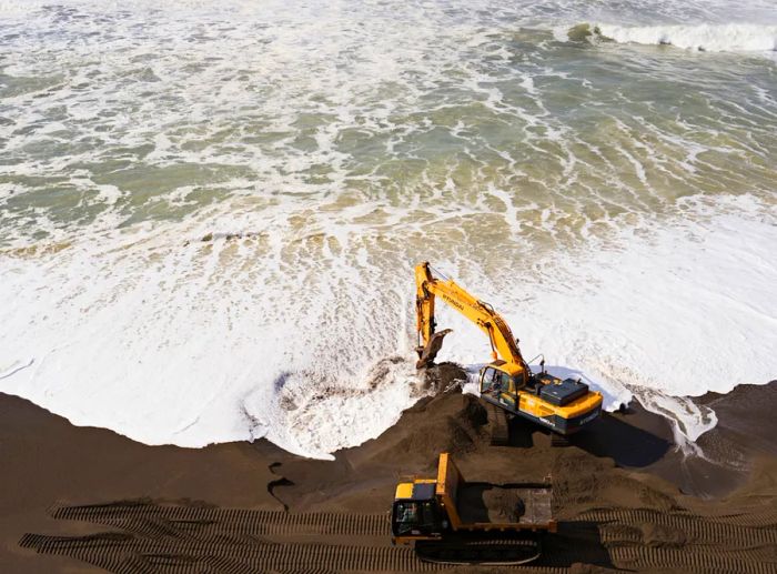 Overhead view of beach restoration efforts carried out by two large machines