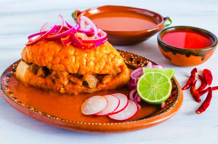 A plate featuring a torta ahogada accompanied by small bowls of red sauces