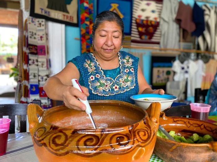 A woman presenting traditional Oaxacan dishes from a clay pot.