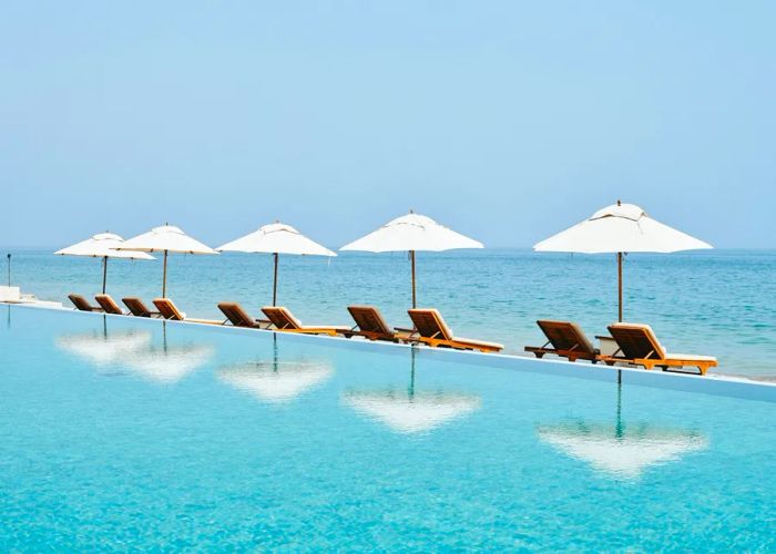 A row of five white umbrellas and unoccupied lounge chairs beside the pool at the Tabacco bar lounge, Chedi Hotel Muscat