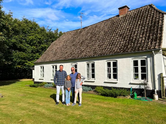 Family standing in front of a white farmhouse in rural Denmark