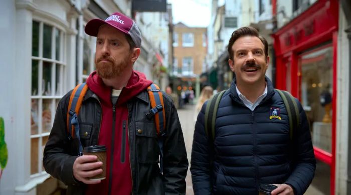 Coach Beard and Ted Lasso stroll down a cobblestone street.