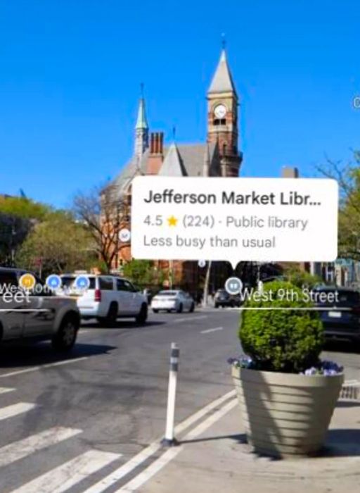 Screenshot of Google Maps showcasing the Lens feature, which overlays icons on buildings as viewed through your phone. This image captures a Manhattan street lined with castle-like brick library structures and a pop-up dialog box identifying the building as Jefferson Market Library.