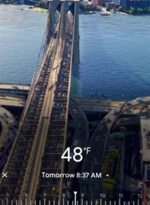 Screenshot of Google Maps on a phone displaying the Immersive View of the Brooklyn Bridge spanning the East River in New York City. The interface includes an overlay showing the current temperature, the time, and a slider that allows users to adjust the time to view the bridge at various times of the day.