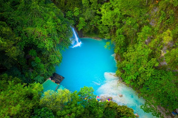 The stunning Kawasan waterfalls nestled in the lush jungle of Cebu Island, Philippines, feature a pool of crystal-clear blue water surrounded by vibrant greenery.