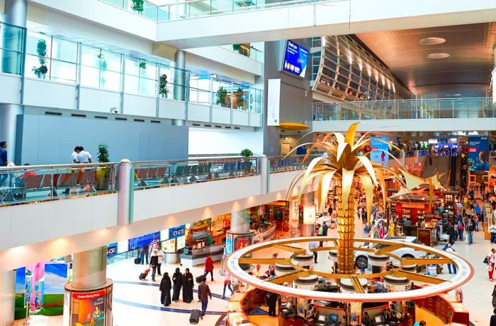 Passengers wandering through a variety of shops and dining options at Dubai International Airport, highlighted by a central golden palm tree sculpture.