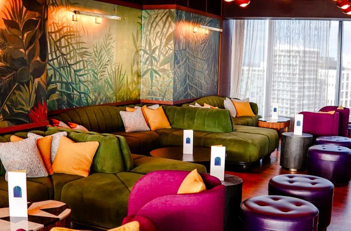 Bar featuring green and pink velvet couches alongside a mural inspired by palm trees