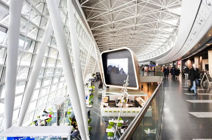 An interior view of Zurich Airport showcasing a large screen and a dining area below