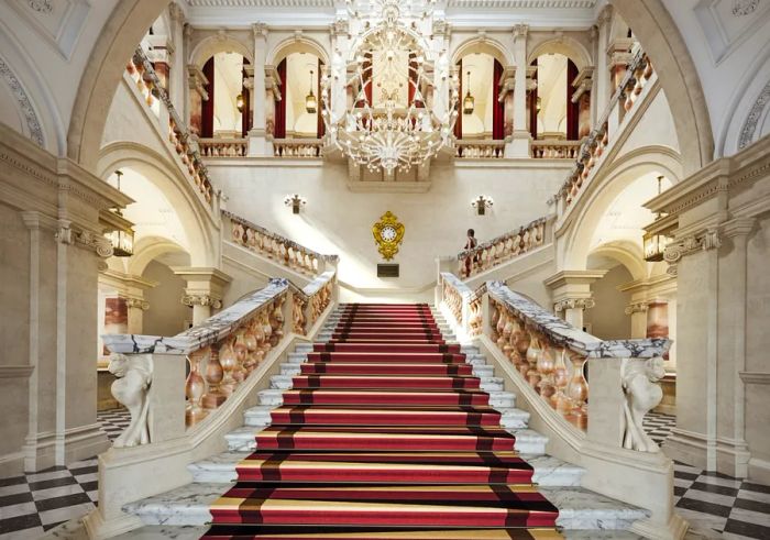 The Grand Staircase at Raffles London at the OWO showcases intricately carved alabaster railings and luxurious marble banisters.