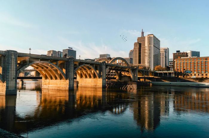 A large bridge leading into Minneapolis–St. Paul (shown) in Minnesota, with several tall office buildings and birds flying overhead.