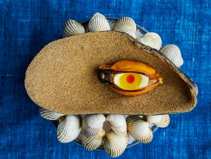 A blue mussel paired with a quail egg presented on a large shell.