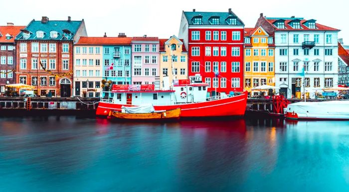 Vibrantly painted houses line a canal, accompanied by a red and white boat.