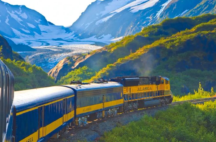 A blue-and-gold train gracefully navigates a bend in front of a massive glacier.