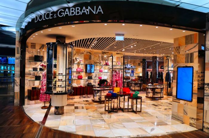 A Dolce and Gabbana store at the airport featuring marble-tiled floors and displays showcasing bags, sunglasses, and apparel