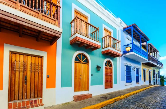 A colorful row of orange, green, blue, and yellow houses, complete with second-story balconies, lines a cobblestone street in Old San Juan, Puerto Rico.