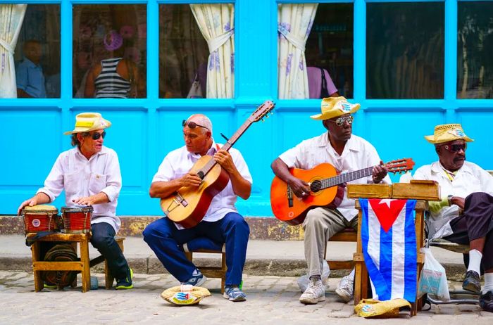 A group of musicians performing on the street in Cuba in front of a vibrant turquoise building.