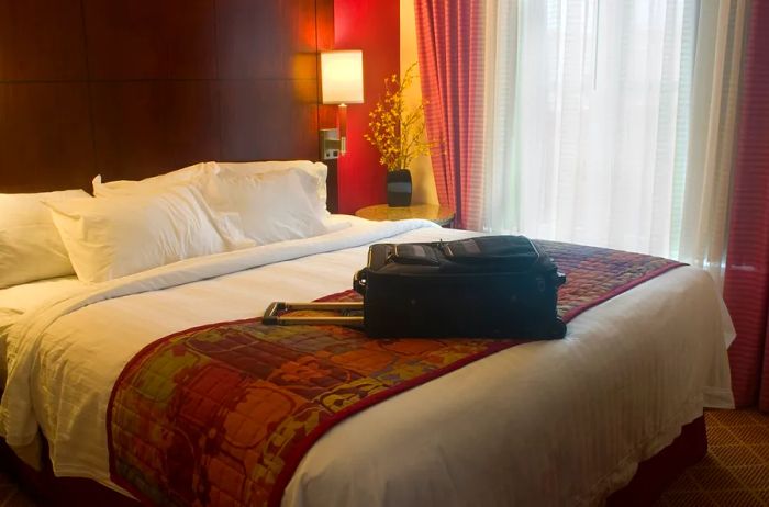 A hotel bed adorned with a throw blanket and a suitcase placed atop it