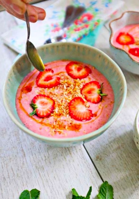 Close-up view of strawberry coconut soup with a spoon drizzling coconut nectar over it.