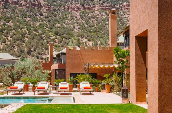 A beautiful riad pool at Kasbah Tamadot, surrounded by pink walls and white lounge chairs.