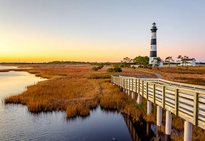 A black and white striped lighthouse standing on marshy land near the water