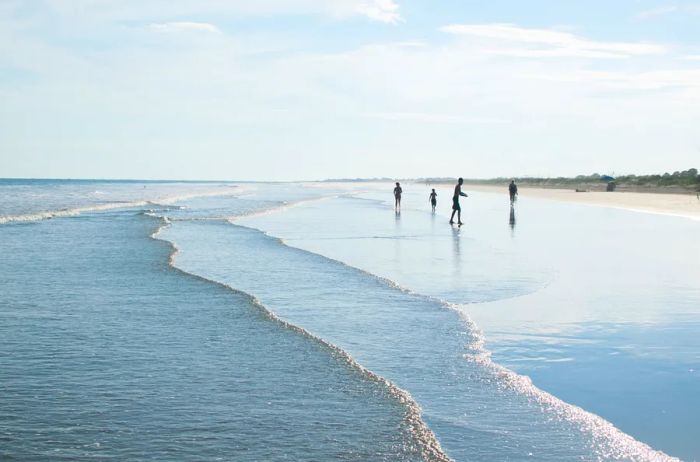 A wide, flat beach with shallow waters, frequented by a few visitors