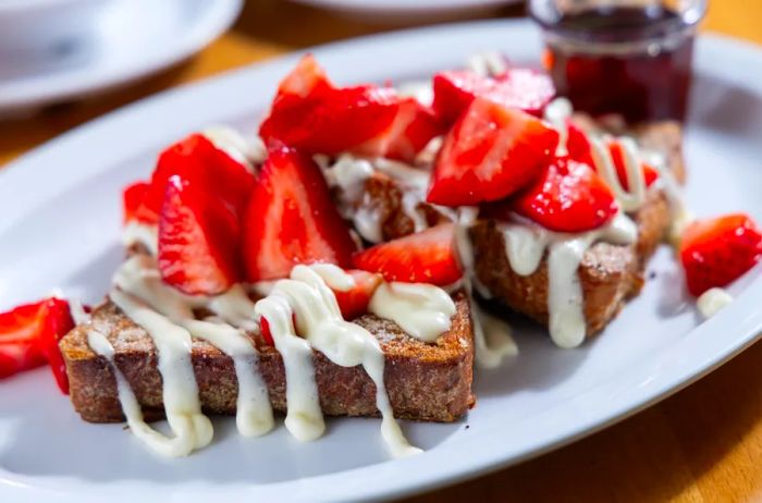 A delicious plate of french toast stacked high with strawberries and drizzled with a creamy topping.