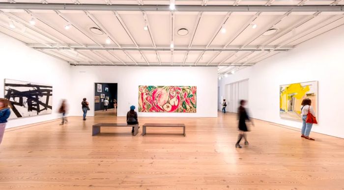 A spacious gallery with white walls, where several visitors admire large modern artworks.