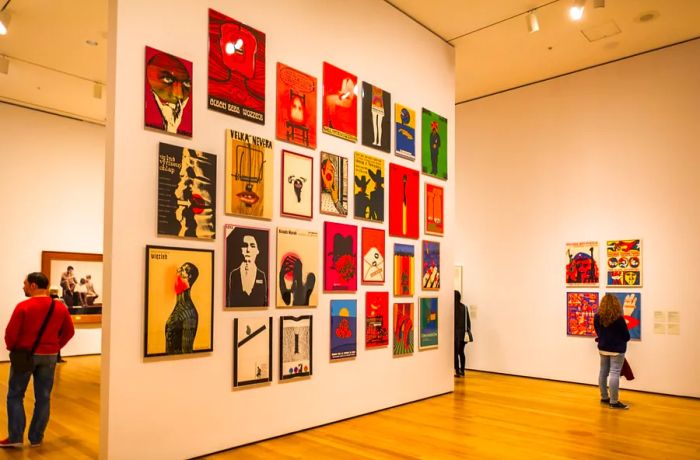 A small group of people admiring colorful vintage posters displayed on white walls in a gallery.