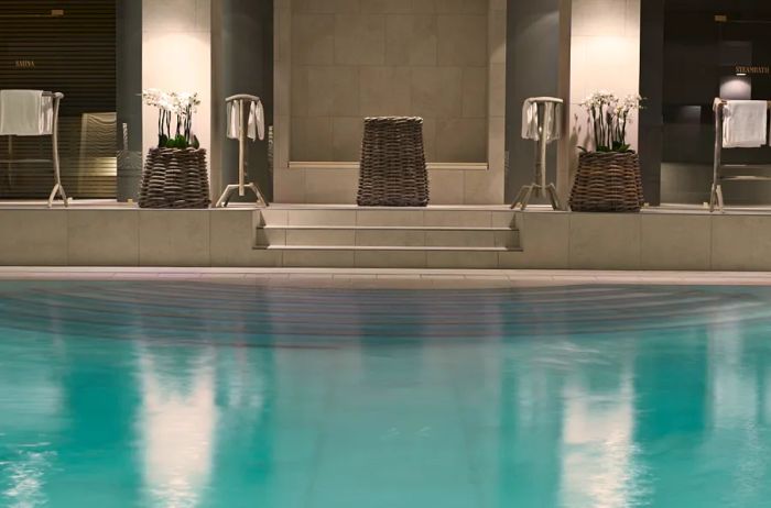 A view from the indoor swimming pool at Hotel D'Angleterre showcases the steps, towel racks, flower arrangements, and a towel disposal basket available for guest use.