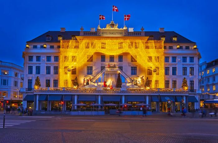 The historic facade of Hotel d'Angleterre in Copenhagen adorned with golden holiday lights, resembling grand stage curtains.