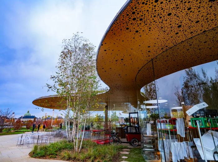 A gracefully curved brown roof dotted with black above expansive floor-to-ceiling windows and greenery.