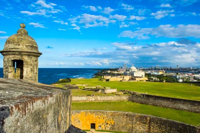 Ancient turret of a fortress overlooking a lush green field with a city in the distance