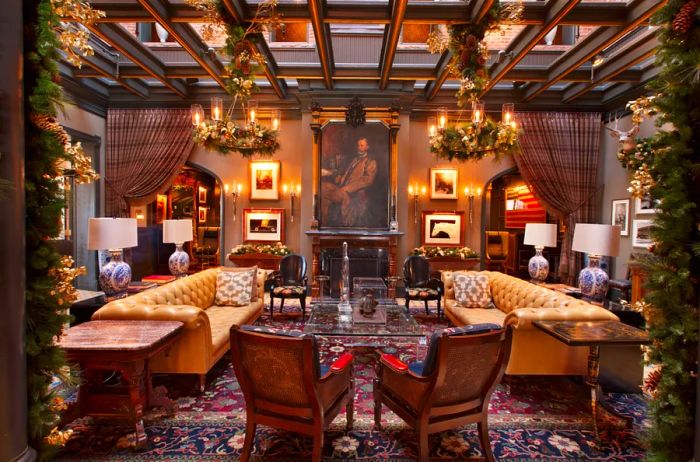 A beautifully designed hotel lobby featuring a framed portrait, two long tufted leather sofas, elegant armchairs, sparkling chandeliers, and festive Christmas decorations, including garlands and ribbons.