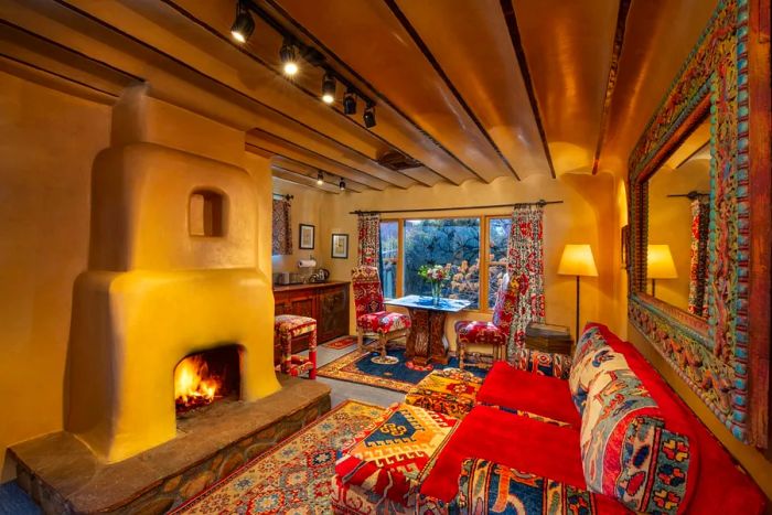 A cozy living area adorned with brightly patterned couches, chairs, and textiles, all centered around a wood-burning adobe kiva fireplace.