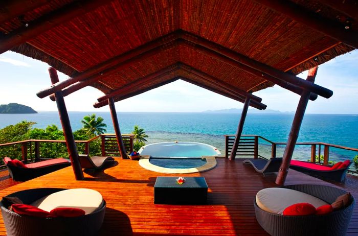 A covered wooden deck with empty white and red chairs facing the Pacific Ocean