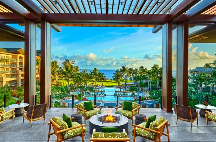 The open-air lobby lanai at the Ritz-Carlton Maui, Kapalua features comfortable seating and a firepit, offering stunning views of the pools, palm trees, and the Pacific Ocean.