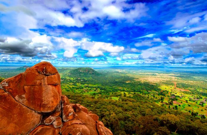 Large red rocks in the foreground, with a lush green forested landscape behind