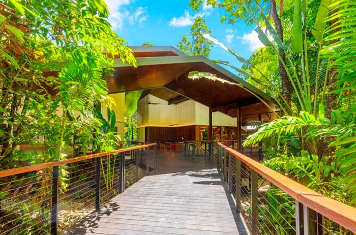 A wooden walkway flanked by greenery leads to the lodge building.