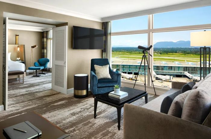 A luxurious taupe Sea Island Suite at Fairmont Vancouver Airport, featuring expansive floor-to-ceiling windows with a view of the runway.